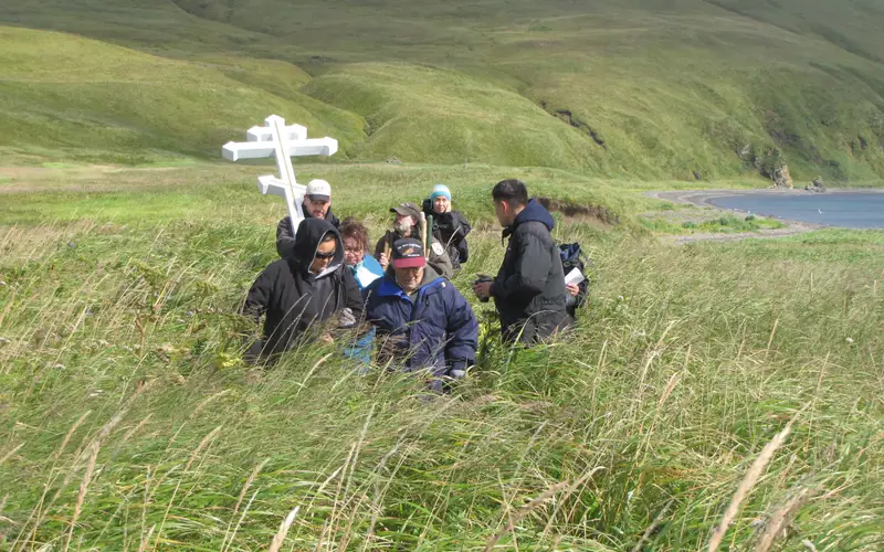 Group of people around a Russian cross in tall grass