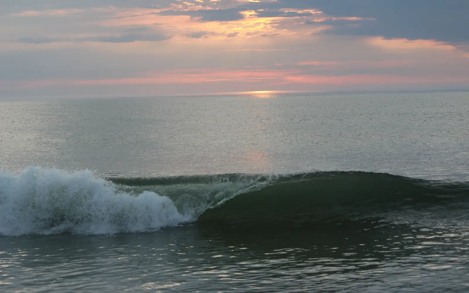 A curling wave breaks against the backdrop of a pink sunrise.