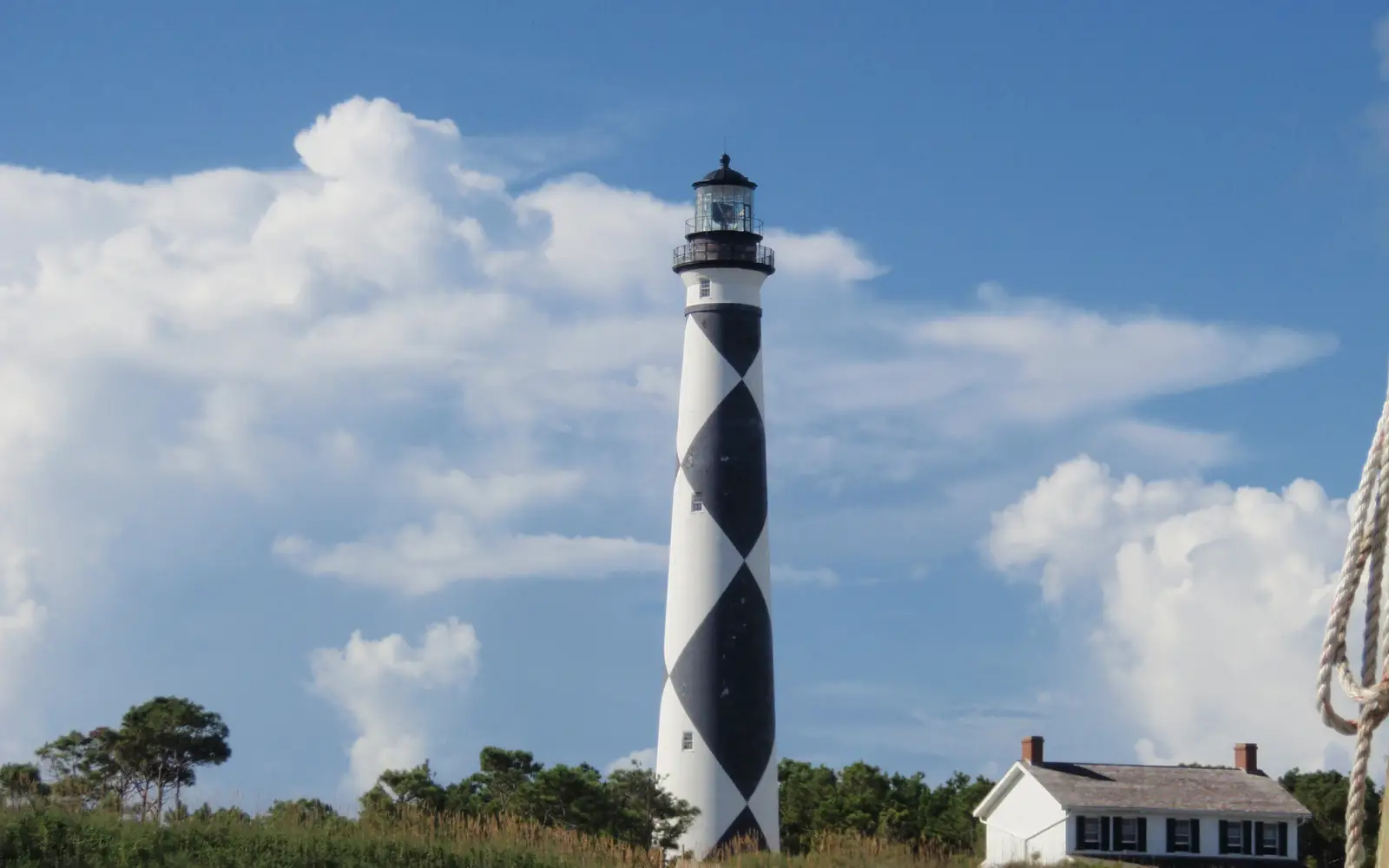 : Black & white patterned tower of the Cape Lookout Lighthouse stands against a blue & white cloud f