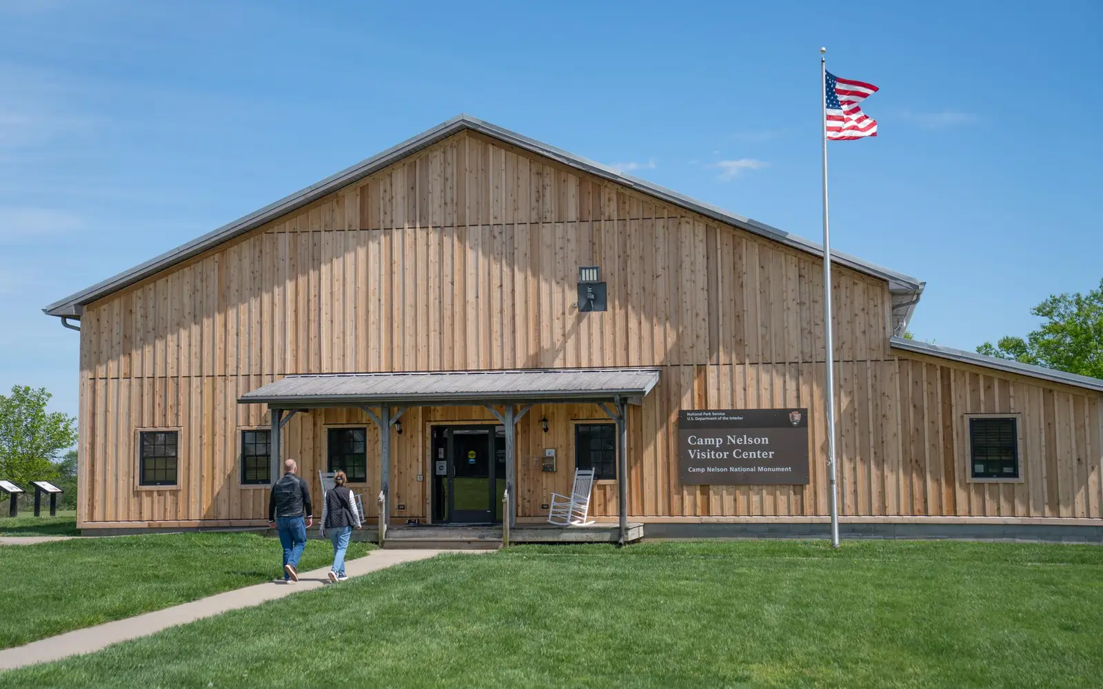 A paved path leads to a gray wooden building with US Flag flying.
