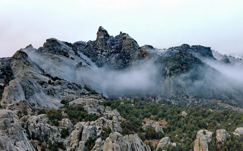 Snow dusted granite formations jut up from a mountainous juniper covered landscape.