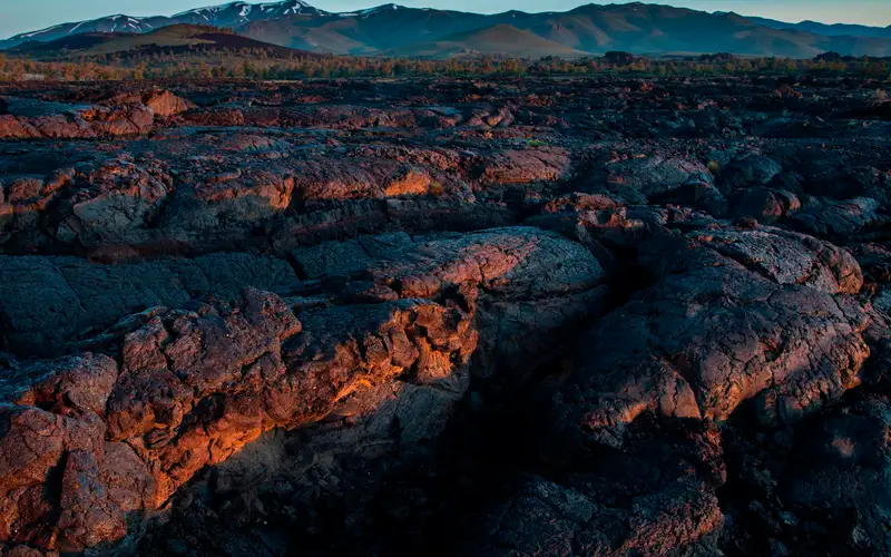A close-up shot of a folded, waving sea of lava rock, with mountains in the far distance.