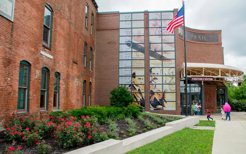 A three-story brick building with tall green windows and a tall photo mural on the glass wall