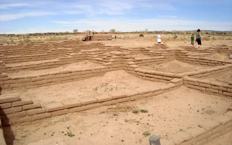 tan-colored pueblo Indian ruins with blue sky and three people