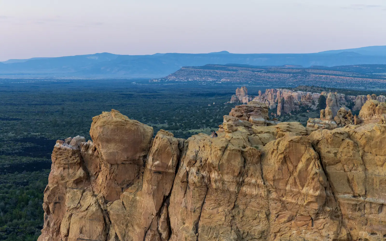 Yellow sandstone cliff at sunset with dark lava field in background