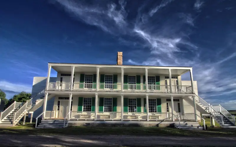 A large two story white building with pillars. Several windows with green shutters