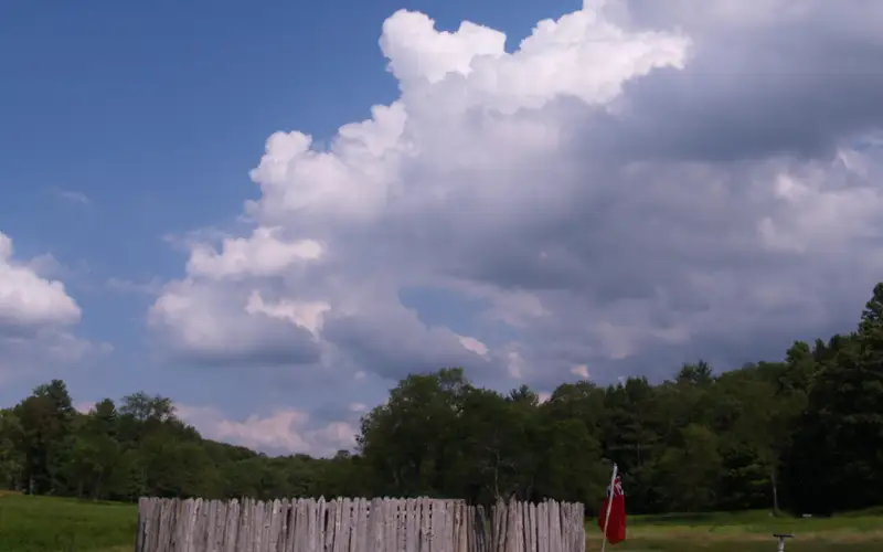 Circular stockade in the middle of a meadow. Dramatic clouds build in the blue sky.