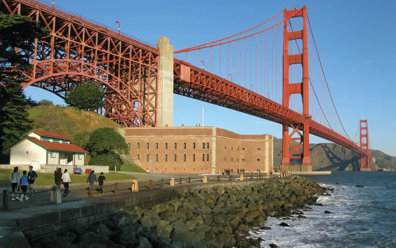 Fort Point with visitors approaching on road in front and Golden Gate Bridge above.