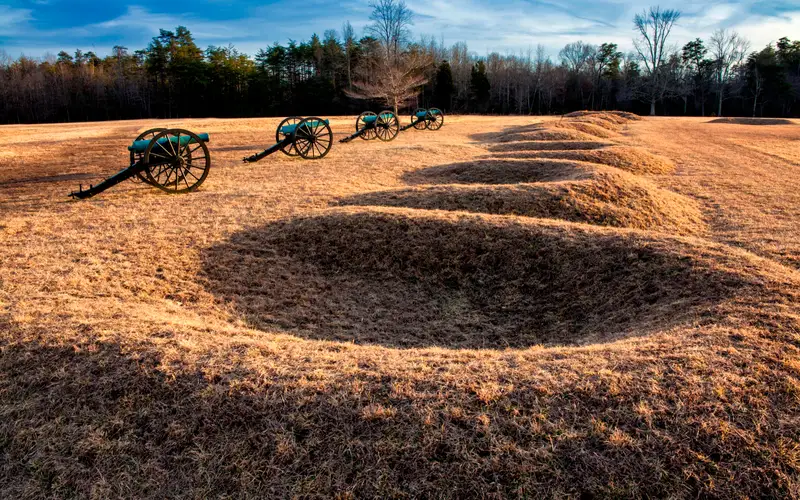 A line of four cannons placed in front of crescent shaped earthen gun pits.