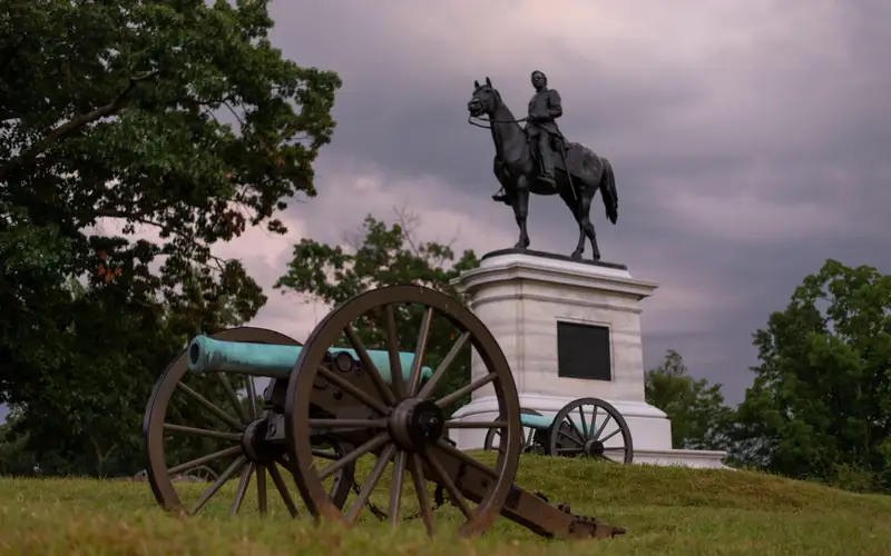 A canon sits in front of an equestrian statue.