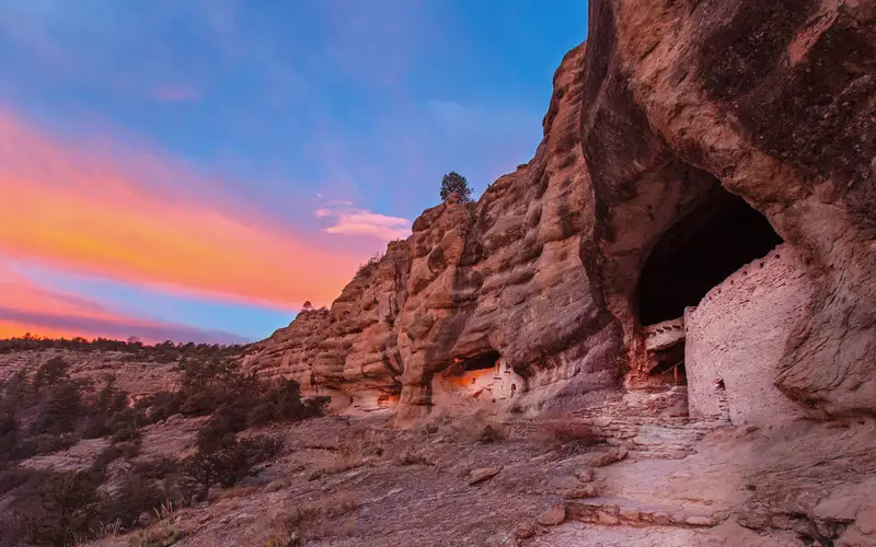 Sunrise view of Gila Cliff Dwellings with brilliant sky.