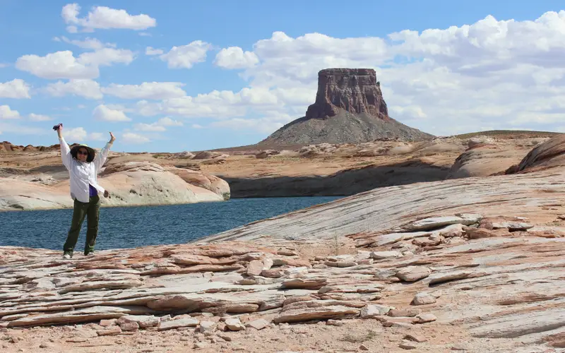 Woman raises her arms while standing in front of a sandstone butte