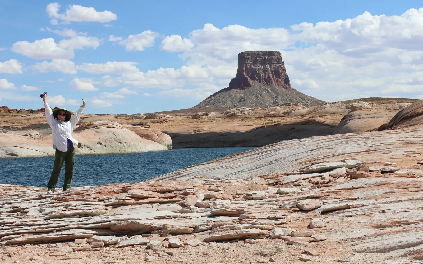 Woman raises her arms while standing in front of a sandstone butte