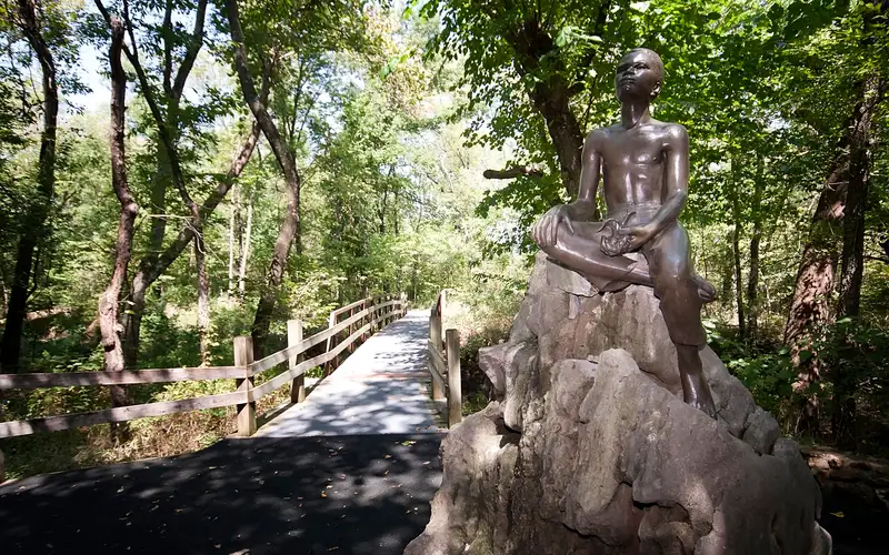 Bronze status of young George Washington Carver atop a large boulder, on the Carver trail.