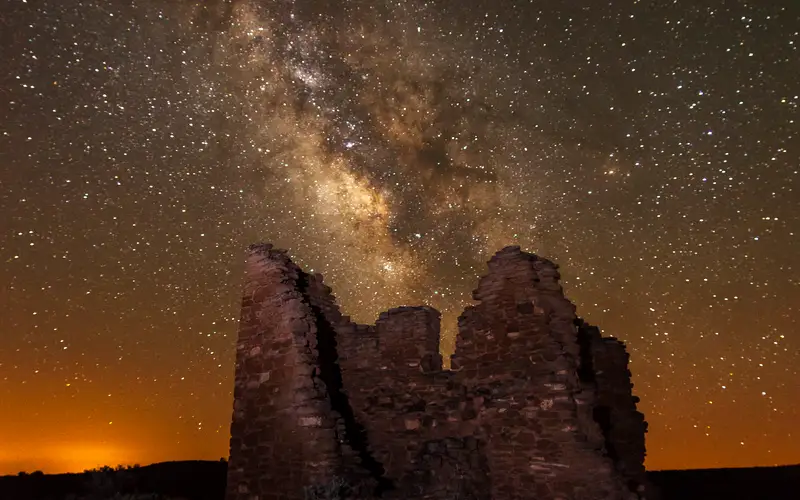 a stone structure at night with the Milky Way arcing overhead