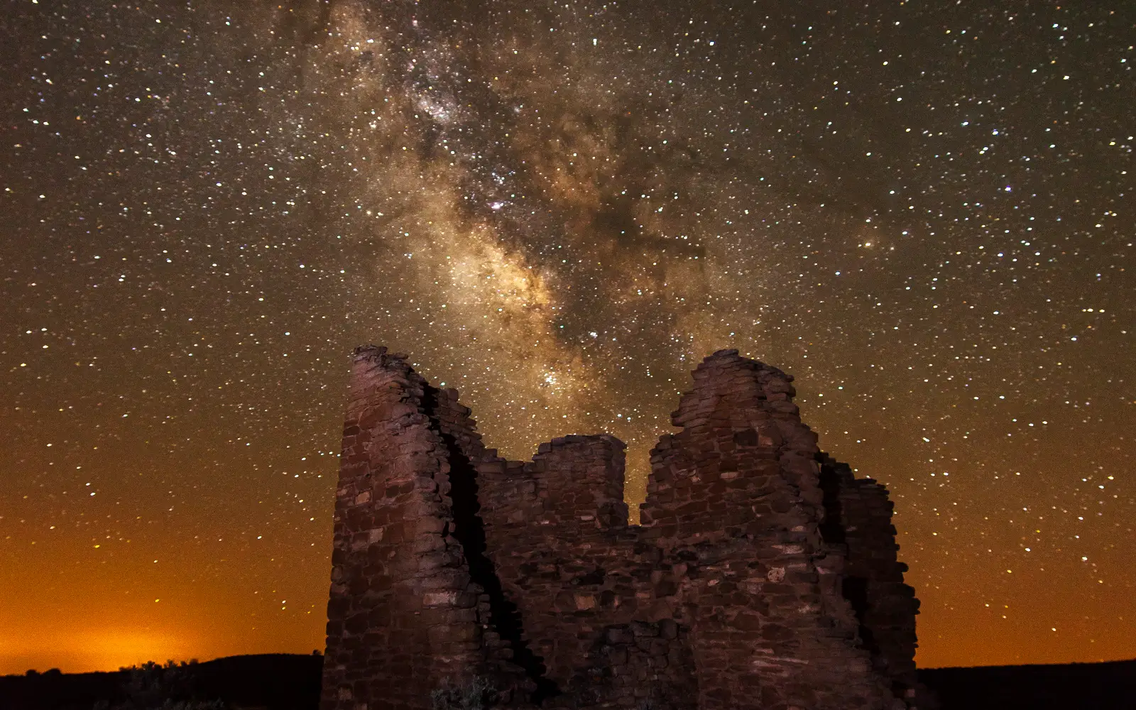 a stone structure at night with the Milky Way arcing overhead