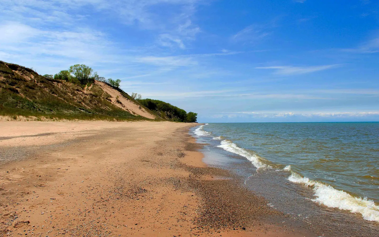 Michigan Lake beach with green grassy dunes in the background, under a blue sky.