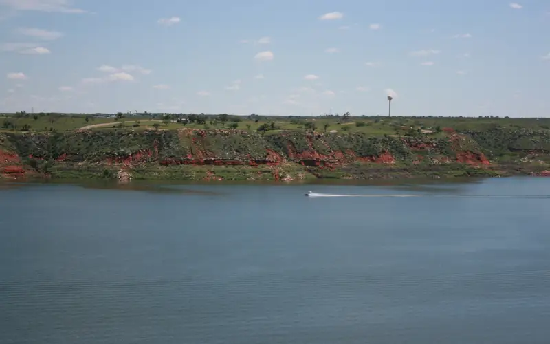 A boat travels across Lake Meredith on a sunny day. The lake is light blue.