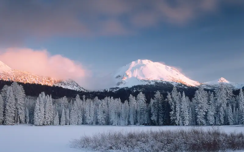 A frozen lake below snow-covered trees and peak