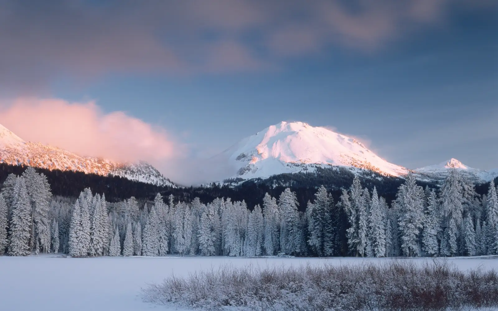 A frozen lake below snow-covered trees and peak