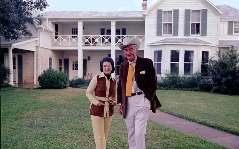 President and Mrs. Johnson stand with their small, white dog in front of the Texas White House.