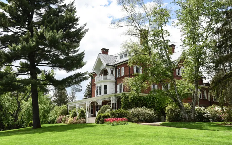 large red brick mansion with white lattice porch and lush green lawn