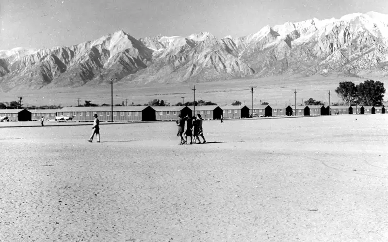 People walk to barracks framed by mountain peaks.