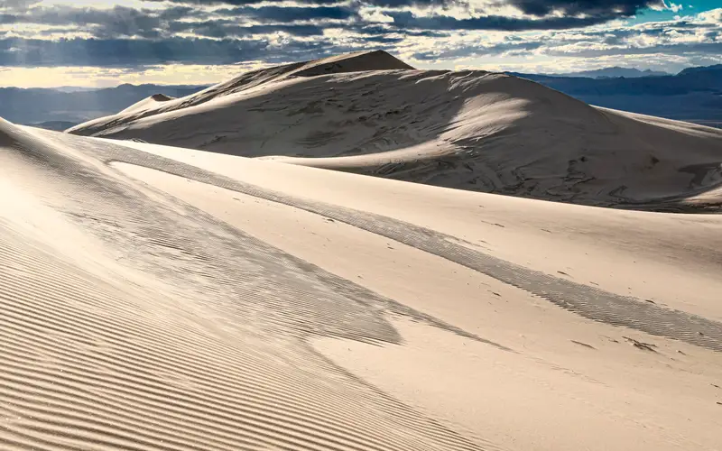 Kelso Dunes with rays of light coming through the clouds. Mountains in the background..