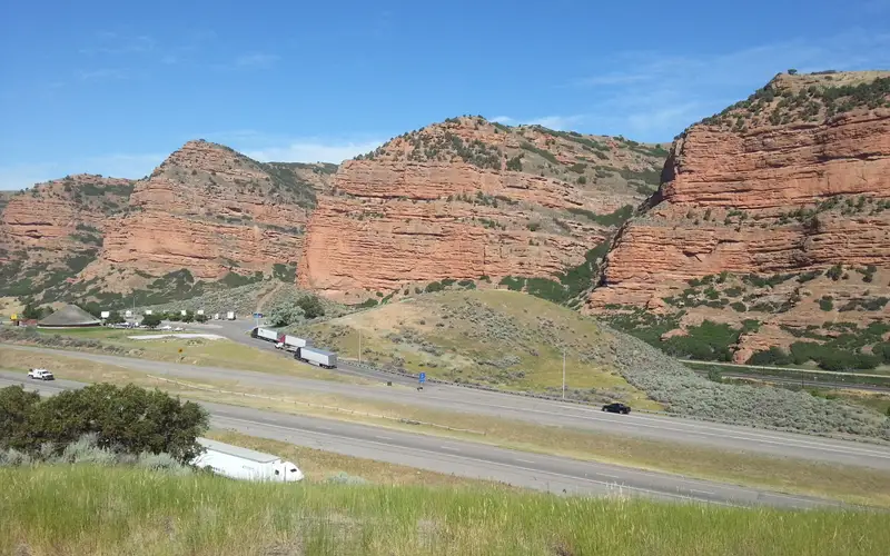 Red cliffs line a highway as seen from a high point with grass in the foreground.