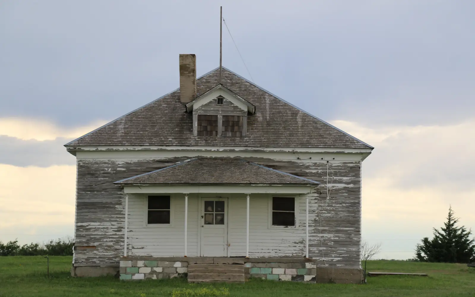Frame one story schoolhouse with most of white paint worn off to show gray.