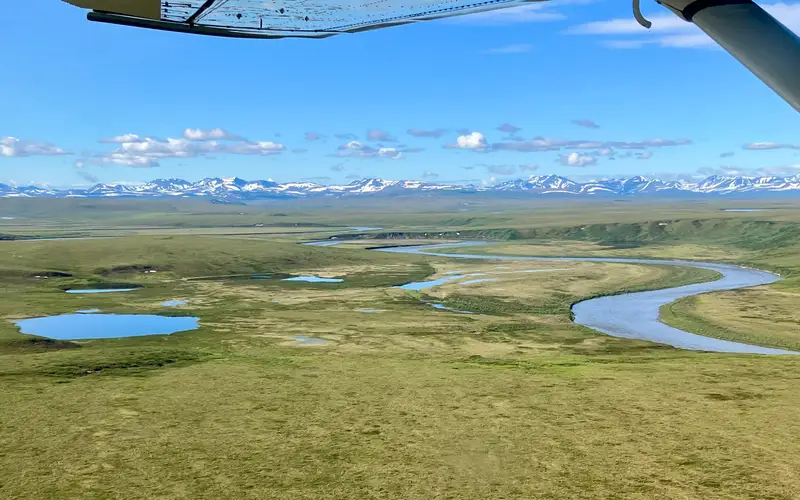 Noatak River cuts through a green tundra landscape with distant mountains.