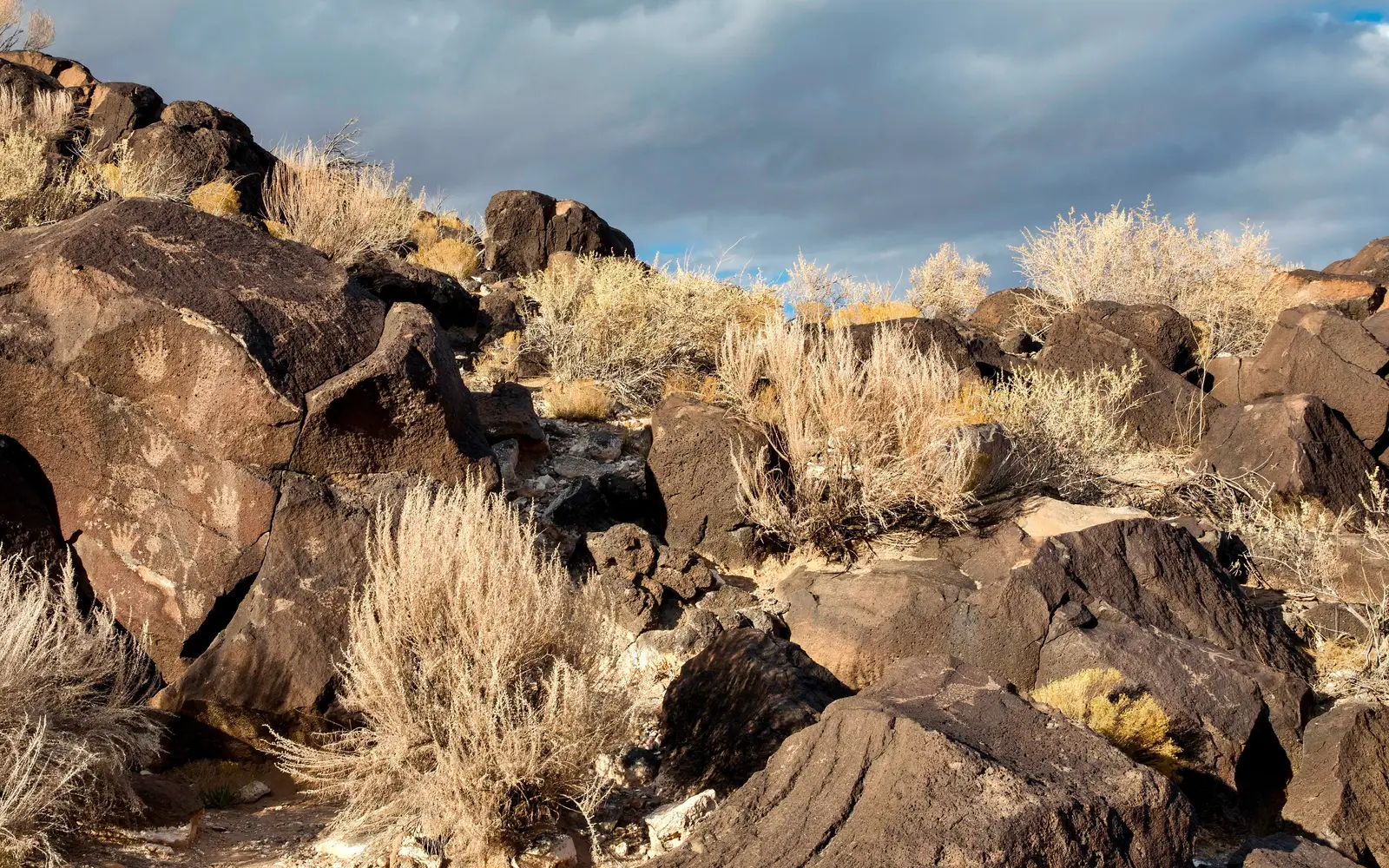 Petroglyphs on dark boulders with a cloudy sky.