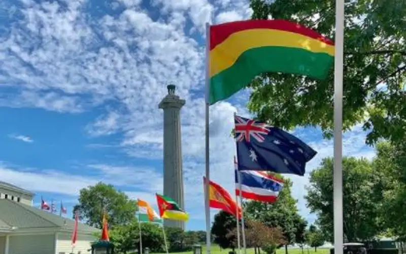 9-3'x5' international flags line sidewalk that leads to a white building with green roof. Tall stone