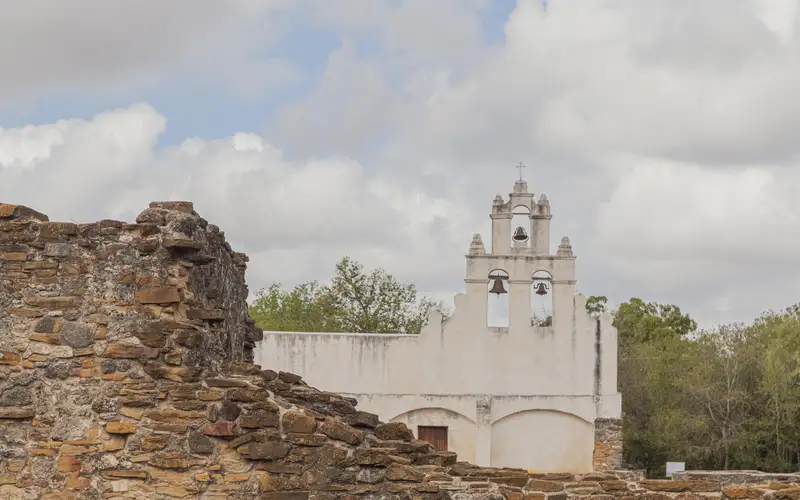 White frescoed church with a stone ruin to the left in the foreground.