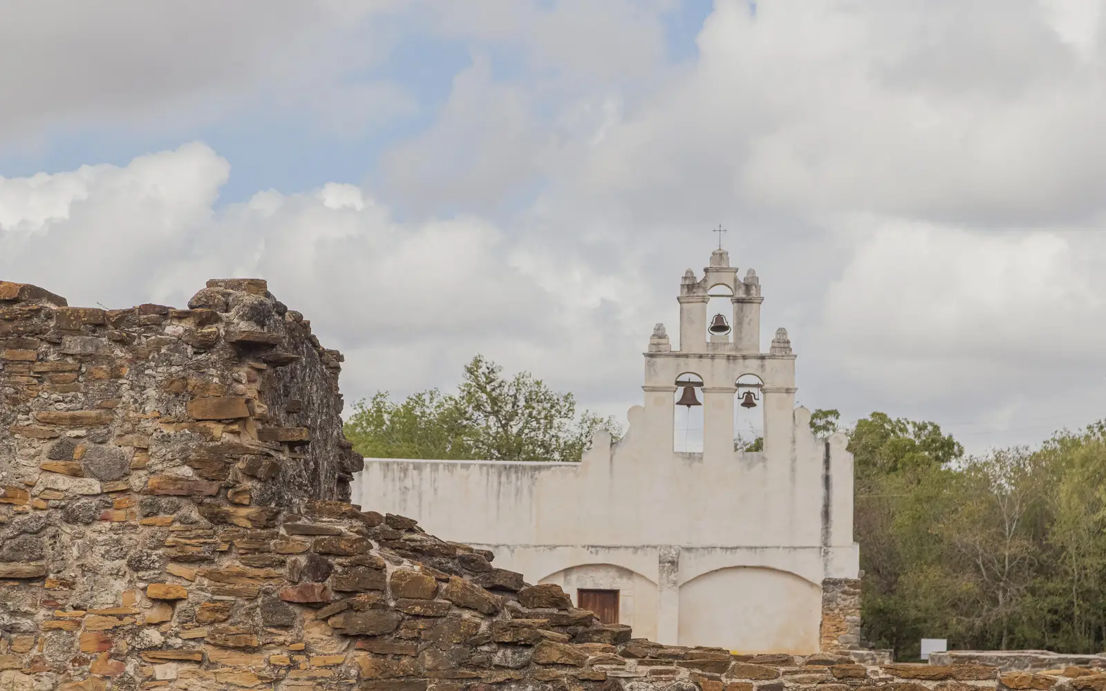 White frescoed church with a stone ruin to the left in the foreground.