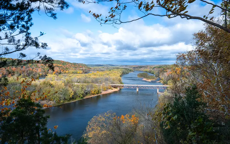 A blue river winds through a valley lined with trees in autumn color.