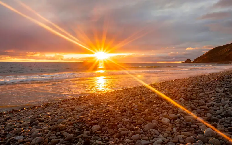 Sunbeams reaching from glowing sun over the ocean.