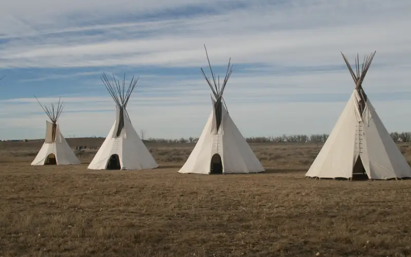 Four white Indian lodges on a grassy plain.