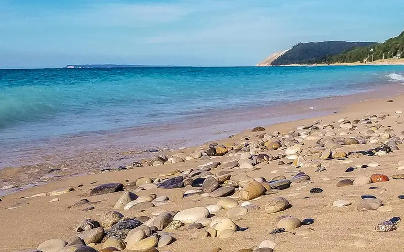 Sand and pebbles in foreground with turquoise water in background