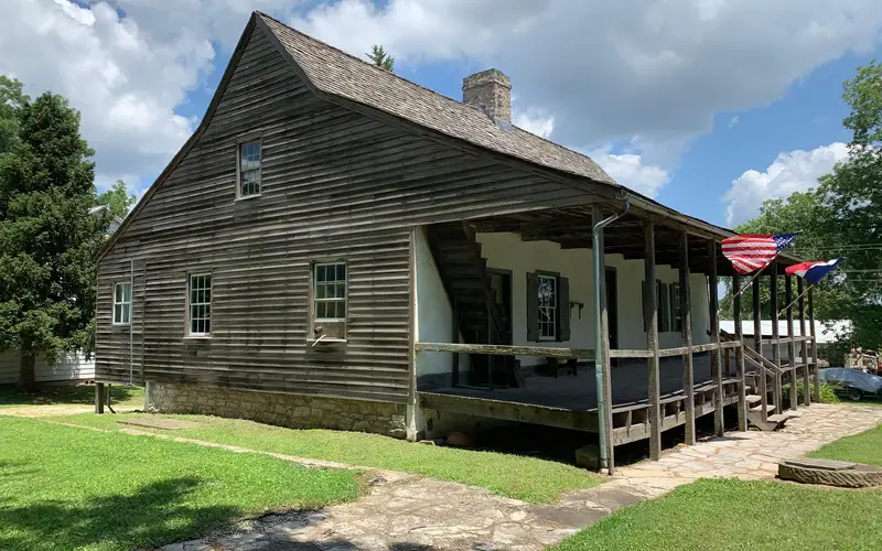 Frame house made of wood with U.S. and French flags flying on front porch.