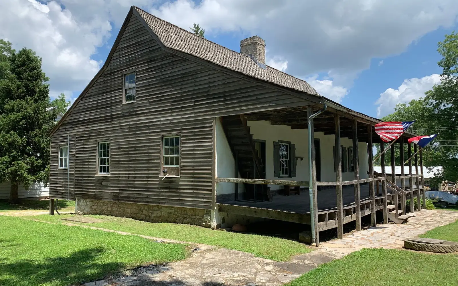 Frame house made of wood with U.S. and French flags flying on front porch.