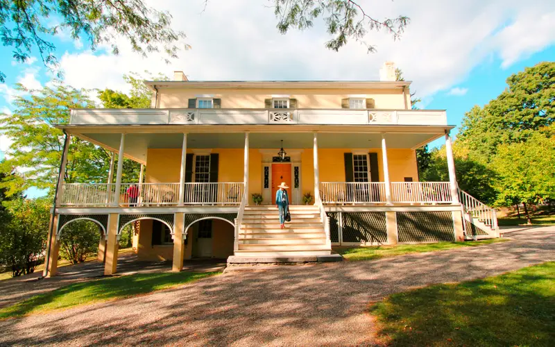 A three story house with large porch across the front and flight of steps leading to the ground.