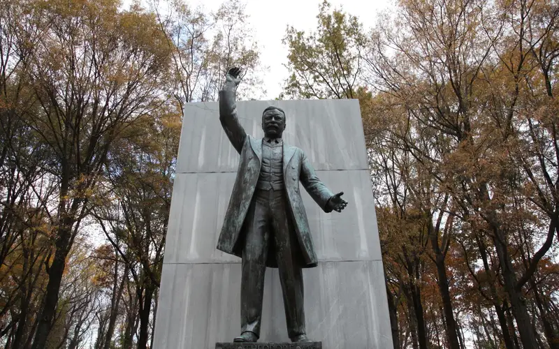 A bronze statue of Theodore Roosevelt standing and pointing.