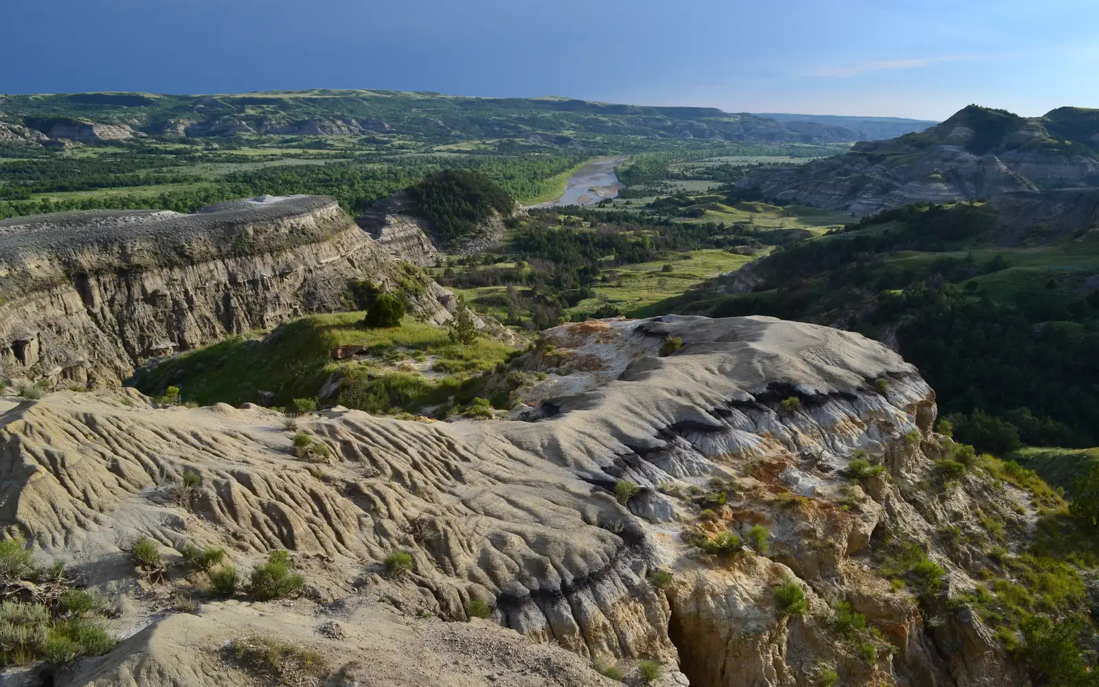 A colorfully striped butte in the foreground overlooks a dark green badlands landscape