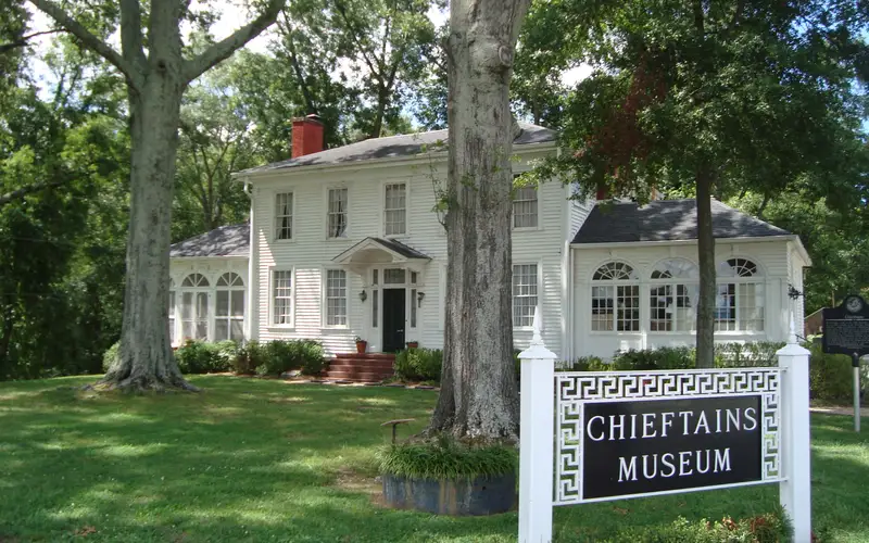 large white house, green lawn, two trees in front