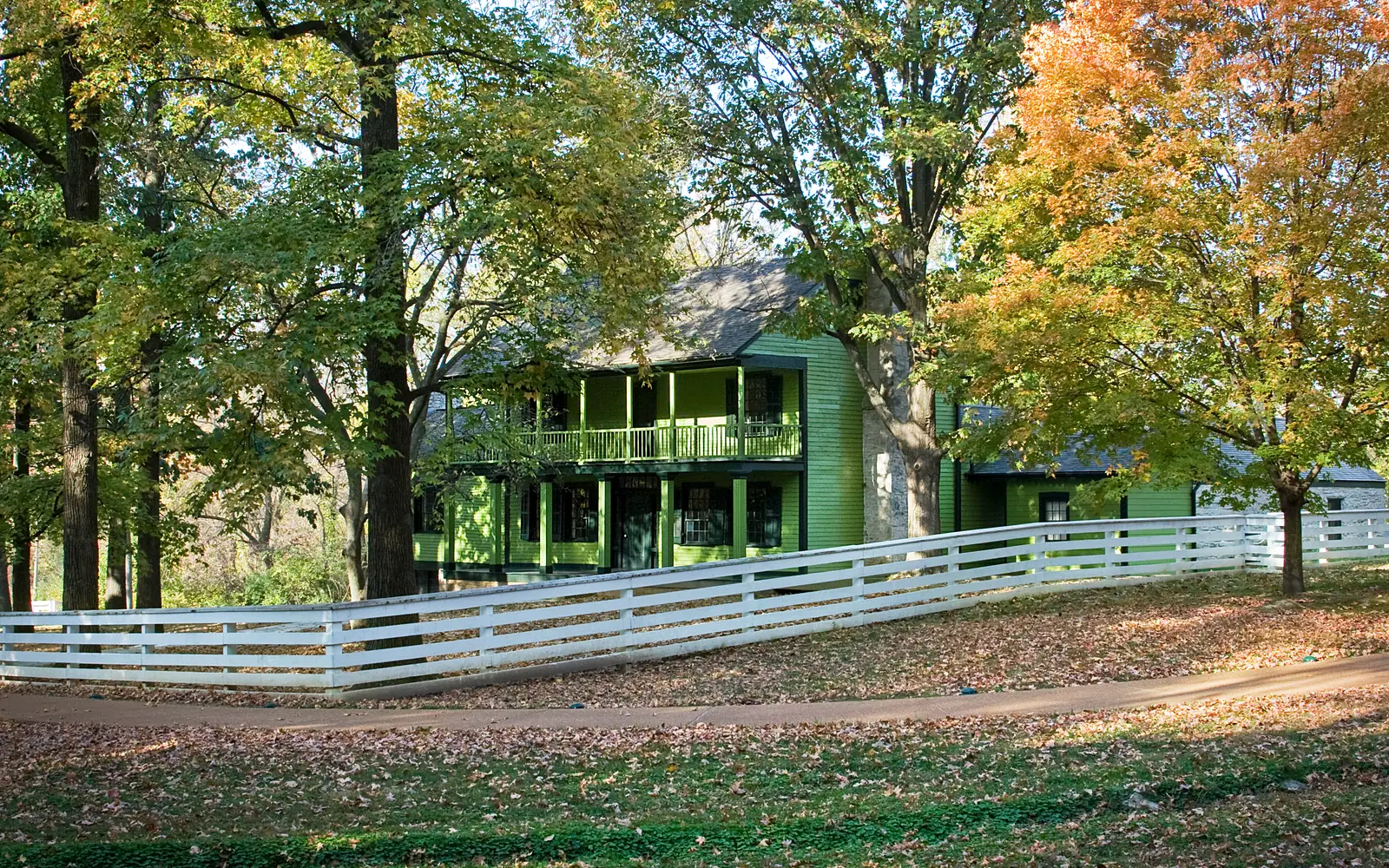 View of house with fence. Autumn colored leaves on trees