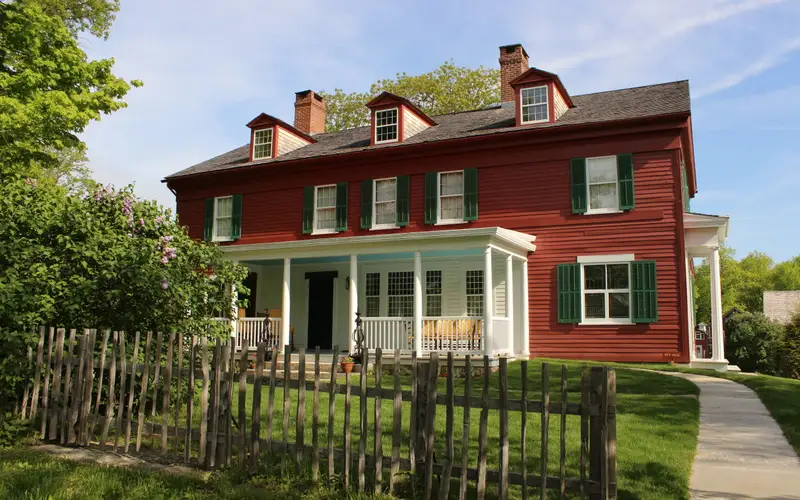 A view of the south side of the Weir House with porch visable, showing a fence in front of the home