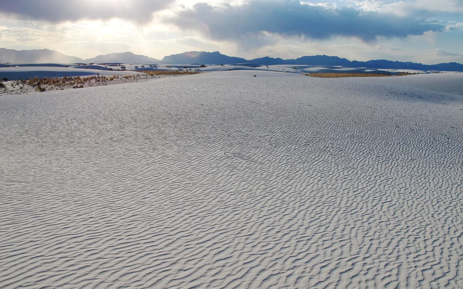 White dunes in foreground with sun setting behind mountain.