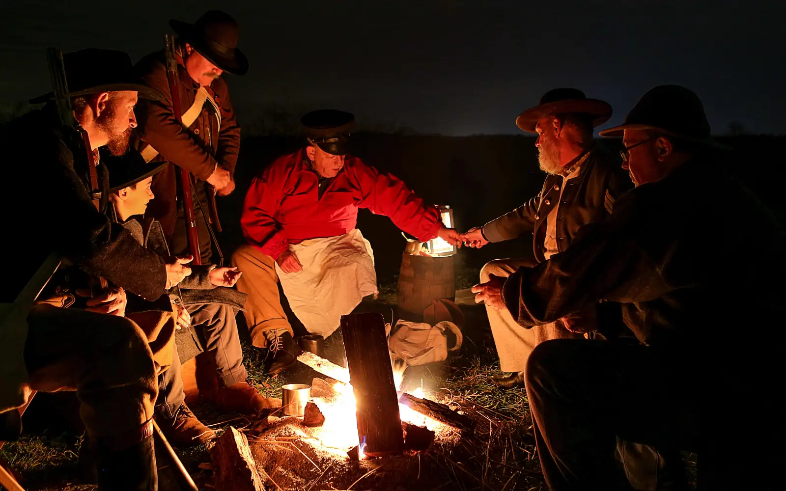 Men in reproduction uniforms talk around a campfire
