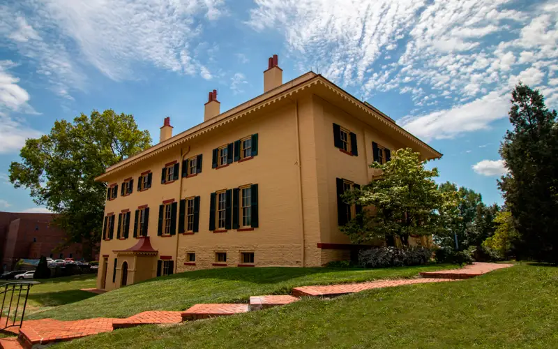 A yellow two-story brick building with tall windows and green shutters on them